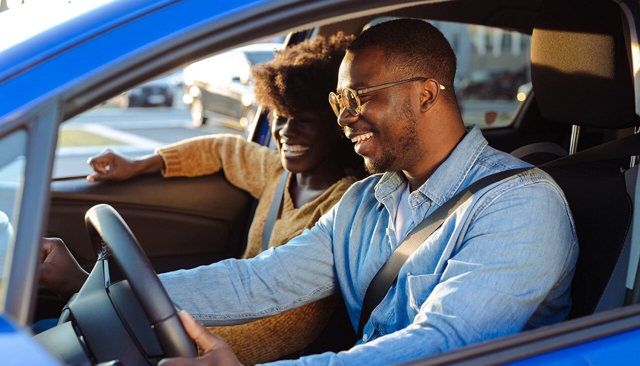 A couple sitting in the front seat of a car preparing to drive away.