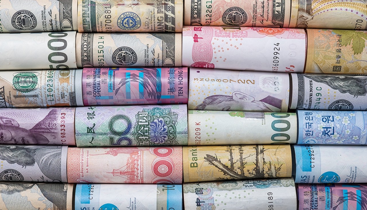 Various foreign currencies are rolled and lined up in rows.
