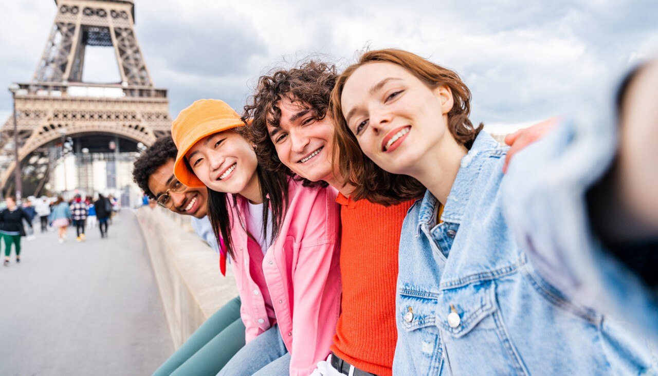 Group of smiling young adult friends smile for a group selfie in front of the Eiffel Tower in Paris, France
